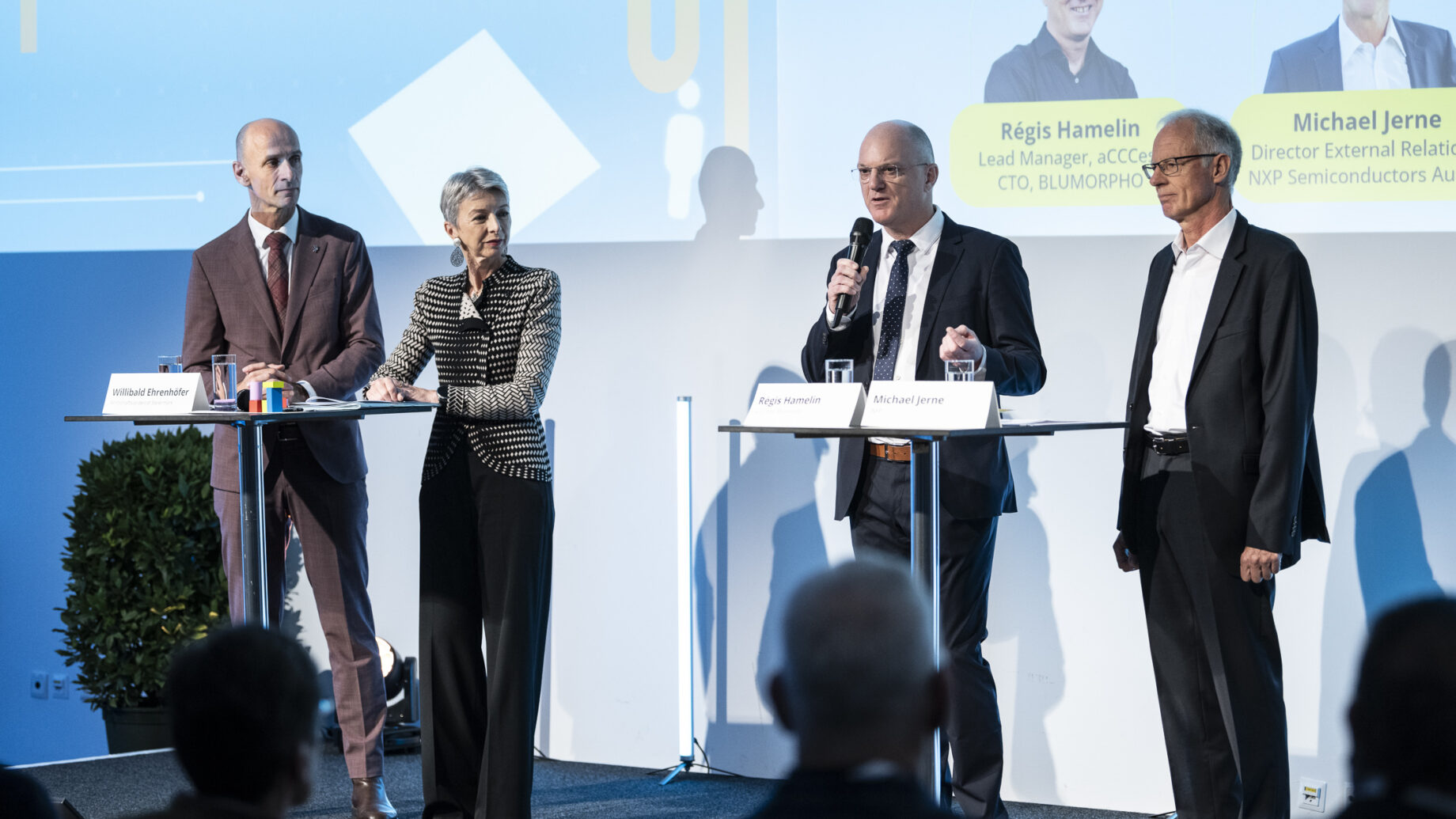 Vier Geschäftsleute sprechen auf der Bühne bei einer Podiumsdiskussion des „Hummelnest Start-up Accelerator Graz“ – mit Mikrofonen und Notizen in der Hand – vor einem blau-weißen Hintergrund.