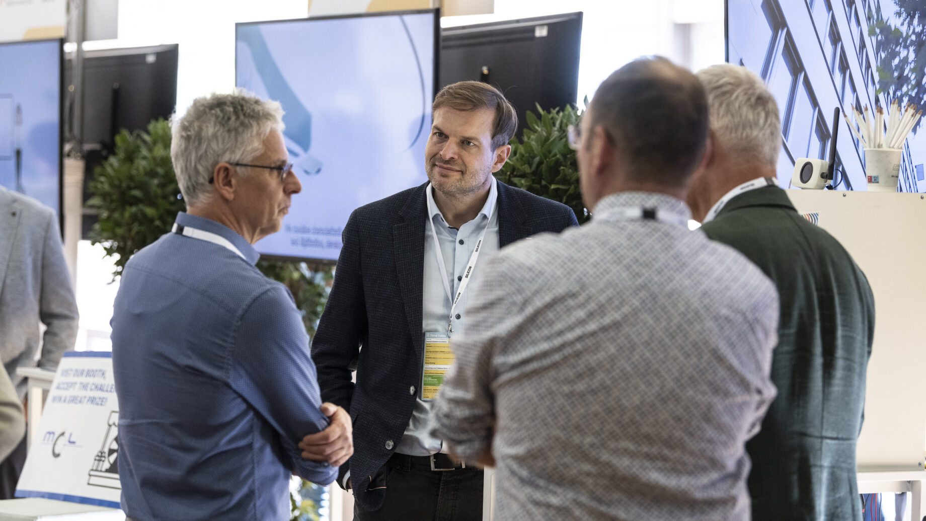 Vier Männer unterhalten sich in einem modernen Büro im Start-up-Accelerator „Hummelnest“ in Graz, hinter ihnen sind Bildschirme und Pflanzen zu sehen. Ein Mann blickt in die Kamera, die anderen haben dem Zuschauer den Rücken zugewandt.