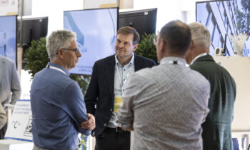 Vier Männer unterhalten sich in einem modernen Büro im Start-up-Accelerator „Hummelnest“ in Graz, hinter ihnen sind Bildschirme und Pflanzen zu sehen. Ein Mann blickt in die Kamera, die anderen haben dem Zuschauer den Rücken zugewandt.