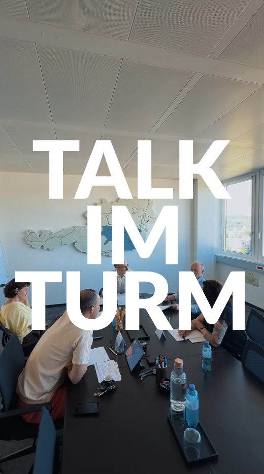 Fünf Personen sitzen um einen modernen Bürotisch herum. Der Text lautet: „TALK IM TURM"