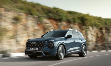 Ein blauer Audi-Geländewagen fährt auf einer kurvigen Straße neben einem felsigen, grünen Hang unter einem klaren Himmel.