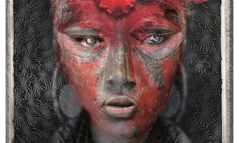 Das Porträt einer Person mit einer roten Blume auf dem Kopf und roter, strukturierter Gesichtsbemalung vor einem gemusterten dunklen Hintergrund.
