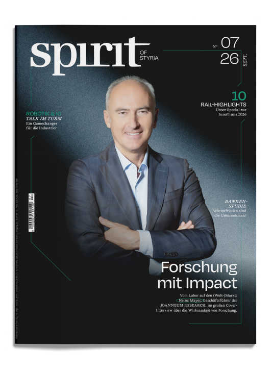 Auf dem Titelblatt des Magazins „Spirit of Styria“, das deutsche Schlagzeilen und einen schwarzen Hintergrund aufweist, steht ein Mann im Anzug mit verschränkten Armen.