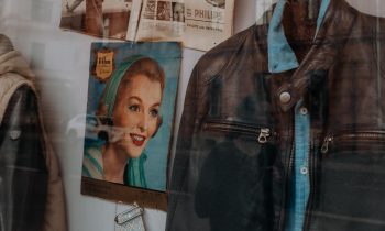 Lederjacke, Hemd, Vintage-Zeitschrift und alte Zeitungen, ausgestellt in einem Schaufenster zusammen mit gelben Blumen und einer gemusterten Krawatte.