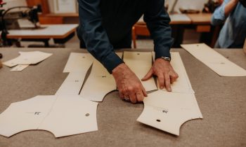 Eine Person legt Schnittmuster aus Papier auf einem Tisch aus und bereitet sich so auf die Herstellung von Kleidungsstücken in einer Werkstatt vor.