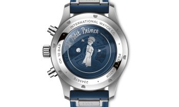 Silberne Uhrenrückseite mit „Le Petit Prince“-Gravur, blauem Armband und einer Illustration des Kleinen Prinzen, umgeben von Sternen und Planeten.