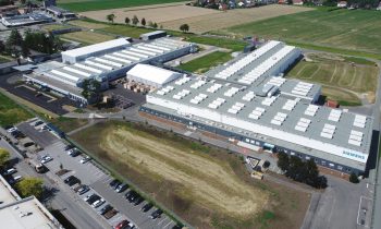 Luftaufnahme einer großen Siemens-Industrieanlage mit mehreren Gebäuden, Parkplätzen und umliegenden grünen Feldern an einem sonnigen Tag.