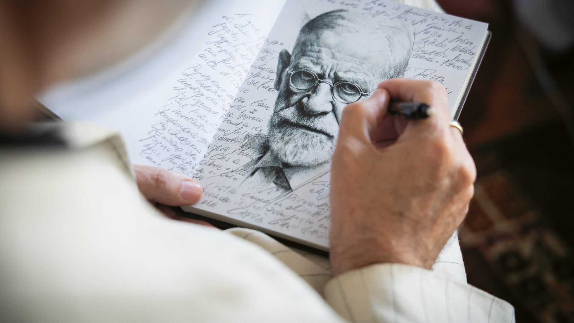 Jemand skizziert das Gesicht eines älteren Mannes in ein Notizbuch, das mit handschriftlichen Notizen gefüllt ist.