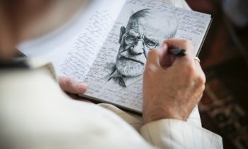 Jemand skizziert das Gesicht eines älteren Mannes in ein Notizbuch, das mit handschriftlichen Notizen gefüllt ist.