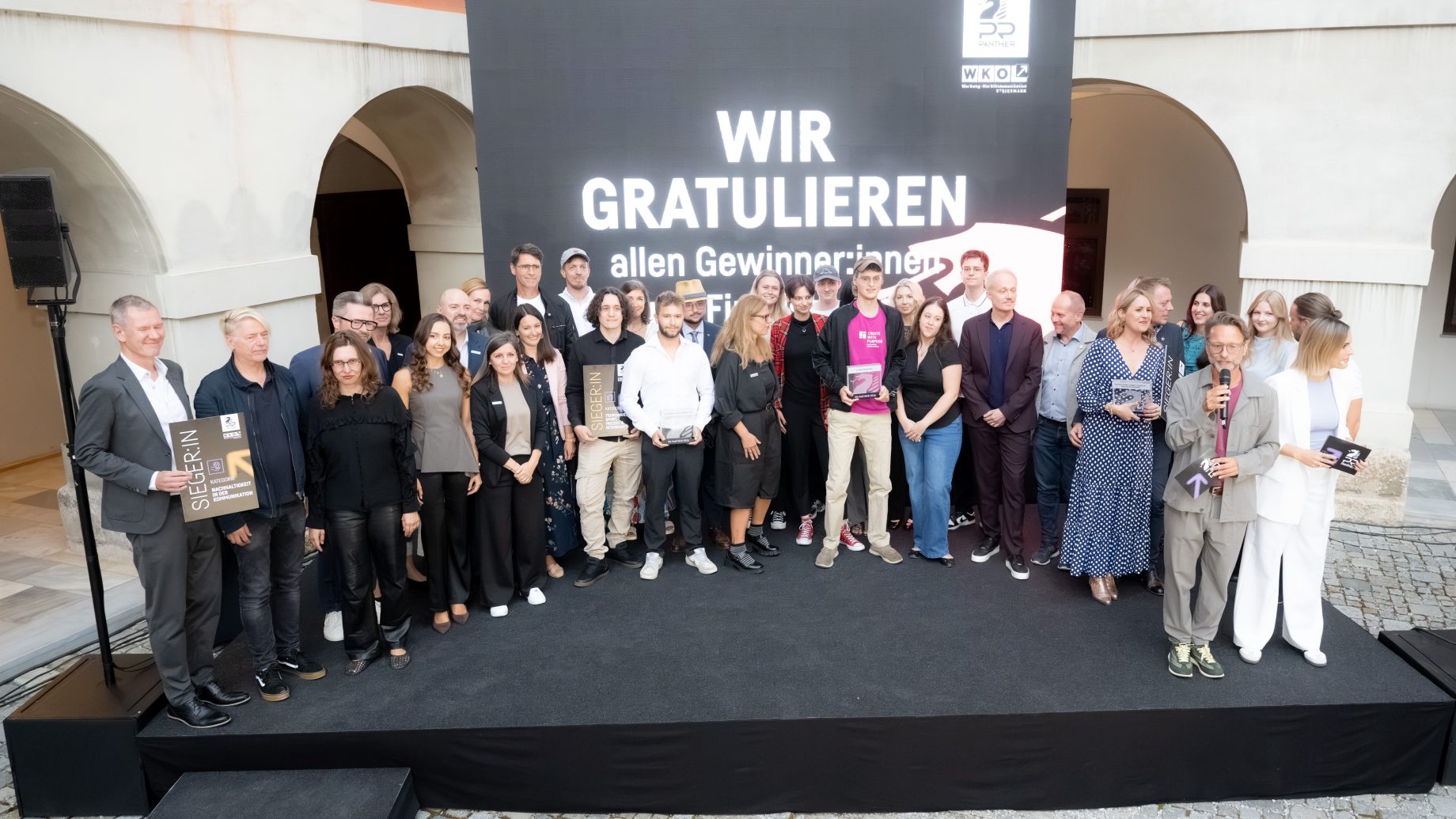 Eine Gruppe posiert auf der Bühne der EBSCON 2026 vor einem Schild mit der Aufschrift „WIR GRATULIEREN“ während einer Preisverleihung.