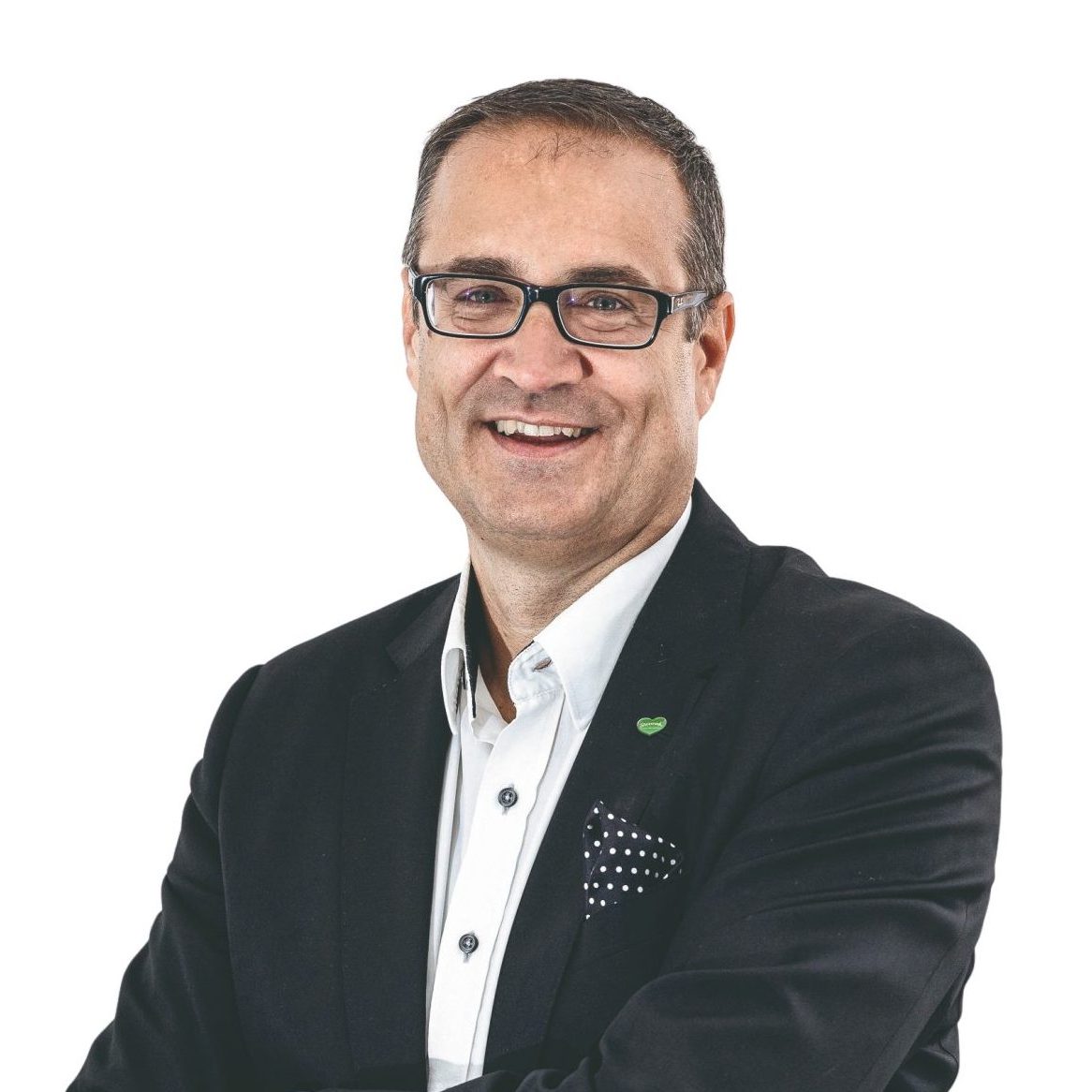 Ein lächelnder Mann im Anzug und mit Brille, der die Arme verschränkt hat.