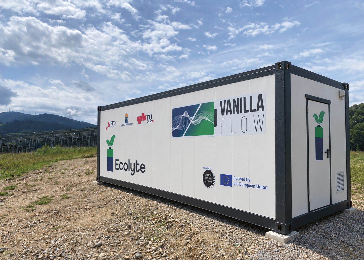 Ein mit „Vanilla Flow“ und „Ecolyte“ beschrifteter Versandcontainer steht unter blauem Himmel auf einem Schotterfeld.