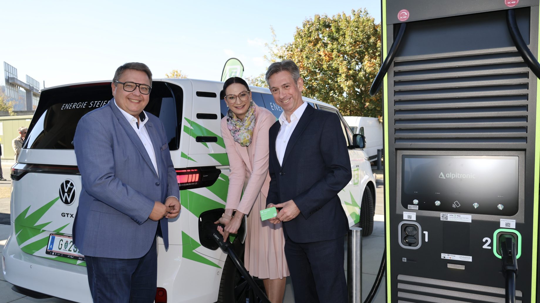 Drei Personen stehen neben einem weißen Volkswagen-Elektrotransporter im neuen Logistikzentrum von Energie Steiermark in Frohnleiten, wobei eine Frau gerade das Kabel einsteckt.