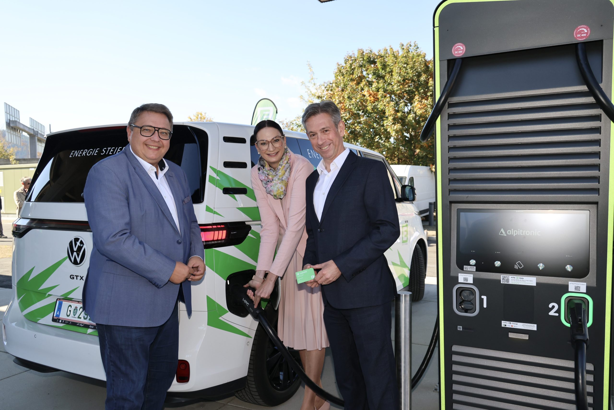 Drei Personen stehen neben einem weißen Volkswagen-Elektrotransporter im neuen Logistikzentrum von Energie Steiermark in Frohnleiten, wobei eine Frau gerade das Kabel einsteckt.