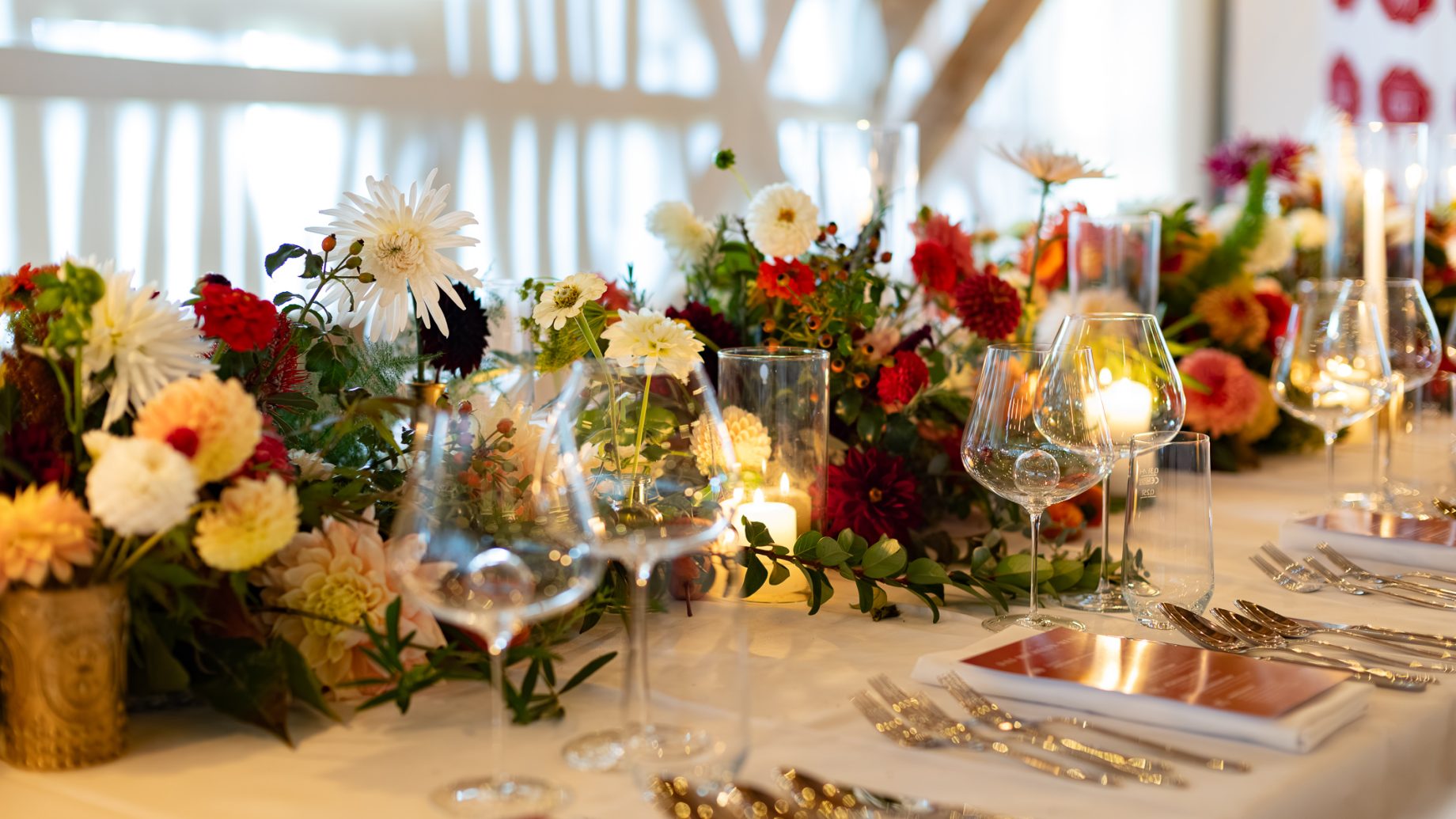 A Der gedeckte Ort, Band 3: Ein Festtagstisch mit Blumengestecken, brennenden Kerzen, Gläsern und Gedecken.