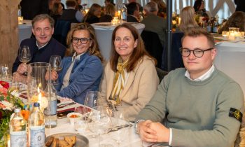 In „Der gedeckte Ort, Band 3“ sitzen vier Personen an einem Tisch in einem Restaurant, auf dem Weingläser, Wasserflaschen und Speisen stehen.