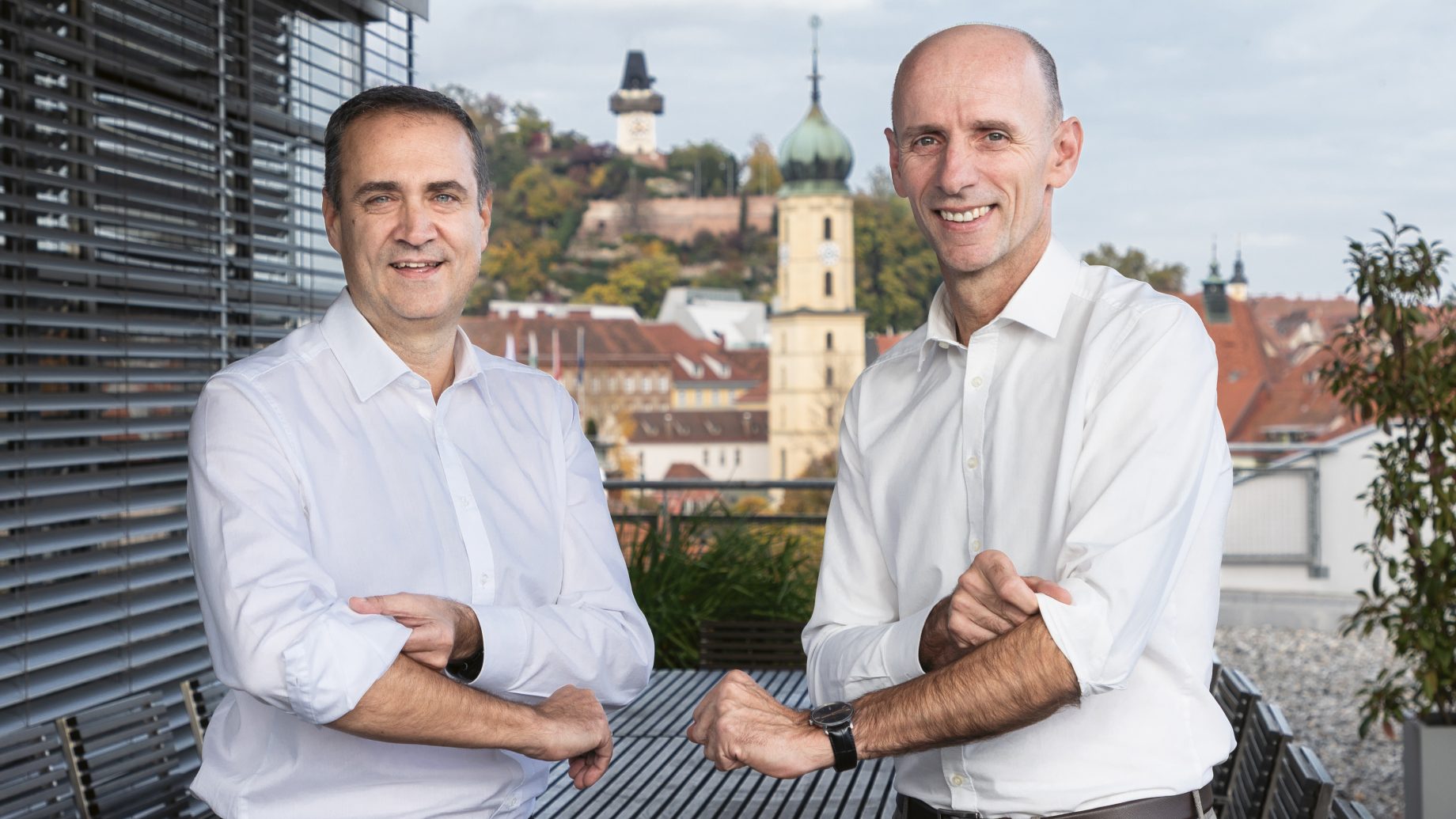Zwei Männer in weißen Hemden stehen auf einem Balkon mit Blick auf die Stadt Graz in Österreich.