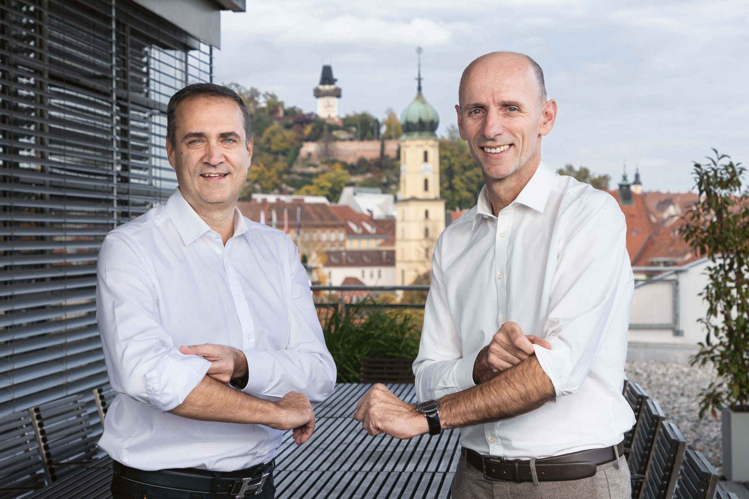 Zwei Männer in weißen Hemden stehen auf einem Balkon mit Blick auf die Stadt Graz in Österreich.
