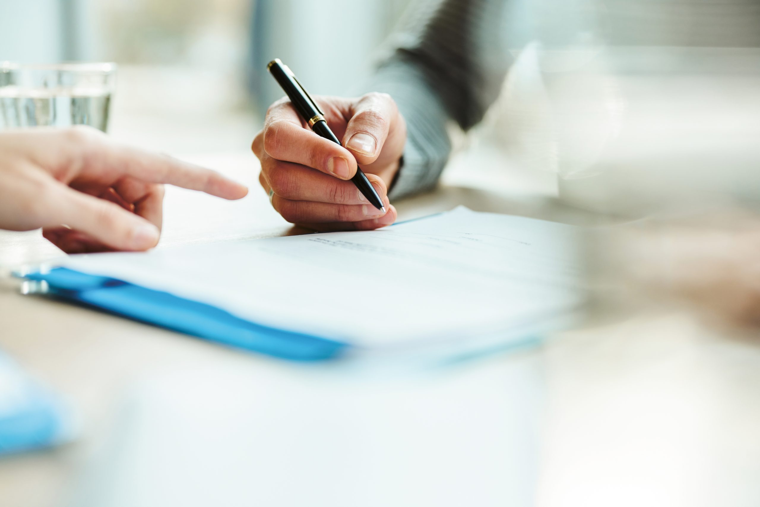 Eine Person zeigt auf ein Dokument, während eine andere Person einen Stift bereit hält, um es zu unterschreiben.