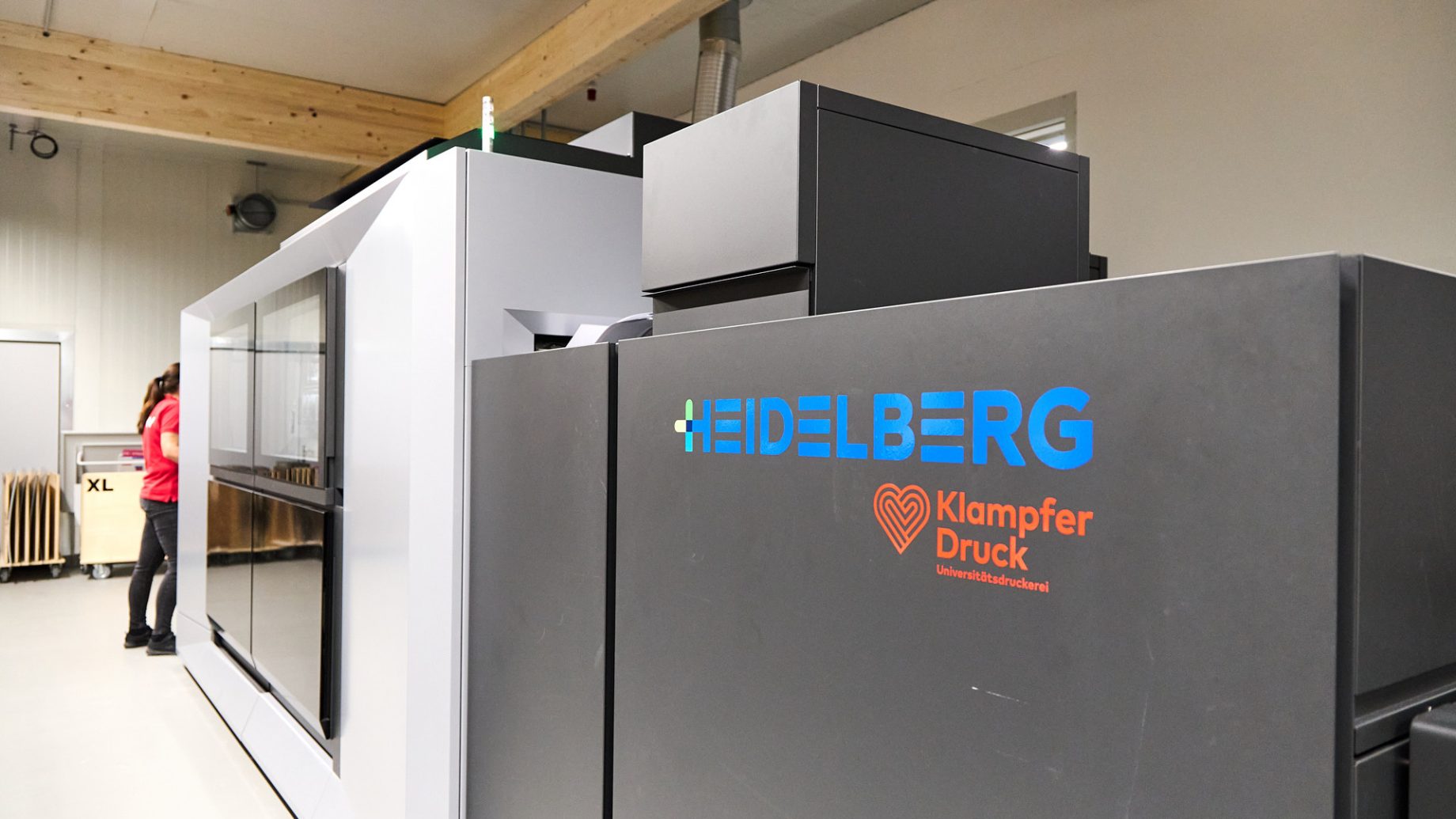 Eine Person steht hinter einer großen Industriedruckmaschine von Heidelberg und Klampfer Druck, was das Engagement für das steirische Energieportfolio verdeutlicht.