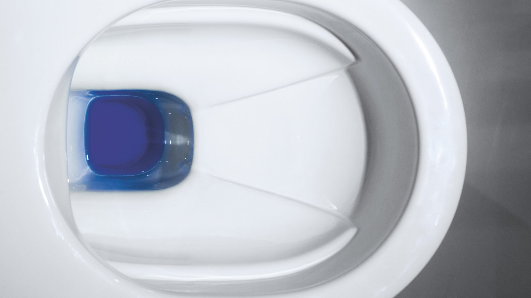 Draufsicht auf eine weiße Toilettenschüssel mit einer blauen Reinigungstablette im Wasser.