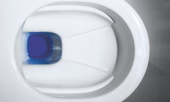 Draufsicht auf eine weiße Toilettenschüssel mit einer blauen Reinigungstablette im Wasser.