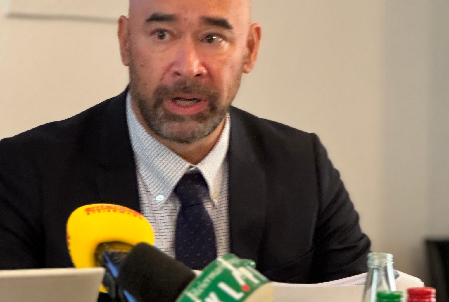 Ein Mann in Anzug und Krawatte spricht auf einer Pressekonferenz von Binder+Co Forschung und Entwicklung, vor ihm stehen mehrere Mikrofone.