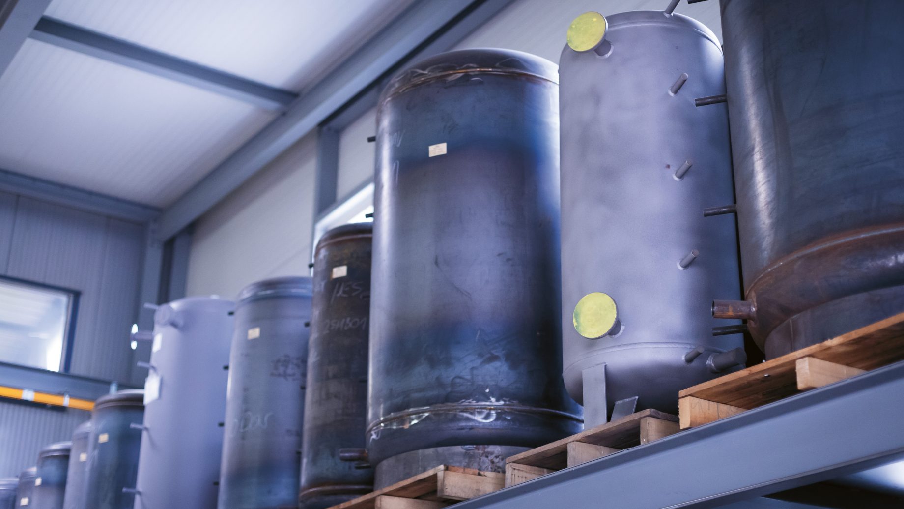 Große industrielle Metalltanks werden aufrecht auf Holzpaletten in einem Hochregal in einem Lagerhaus gelagert.