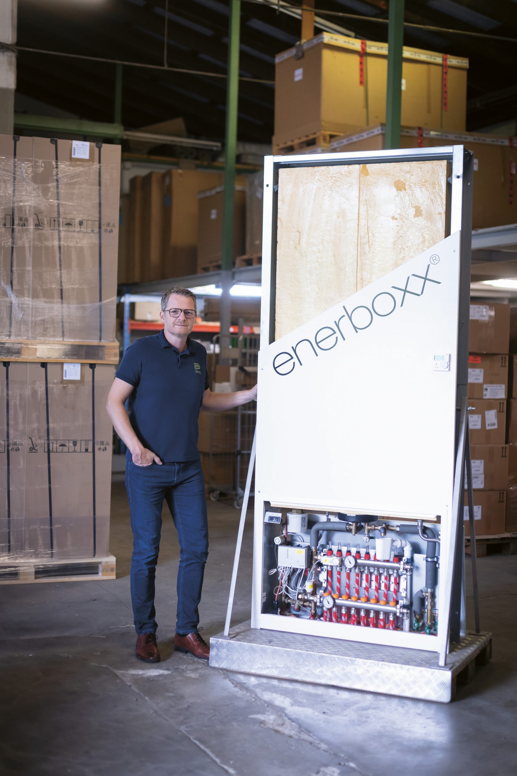 Ein Mann steht neben einer großen Enerboxx-Industrieanlage in einem Lagerraum, der mit Kartons und Regalen gefüllt ist.