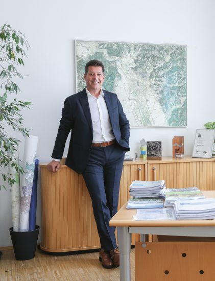 Ein Mann im Anzug, der in einem Büro steht und sich an einen Holzschrank lehnt.