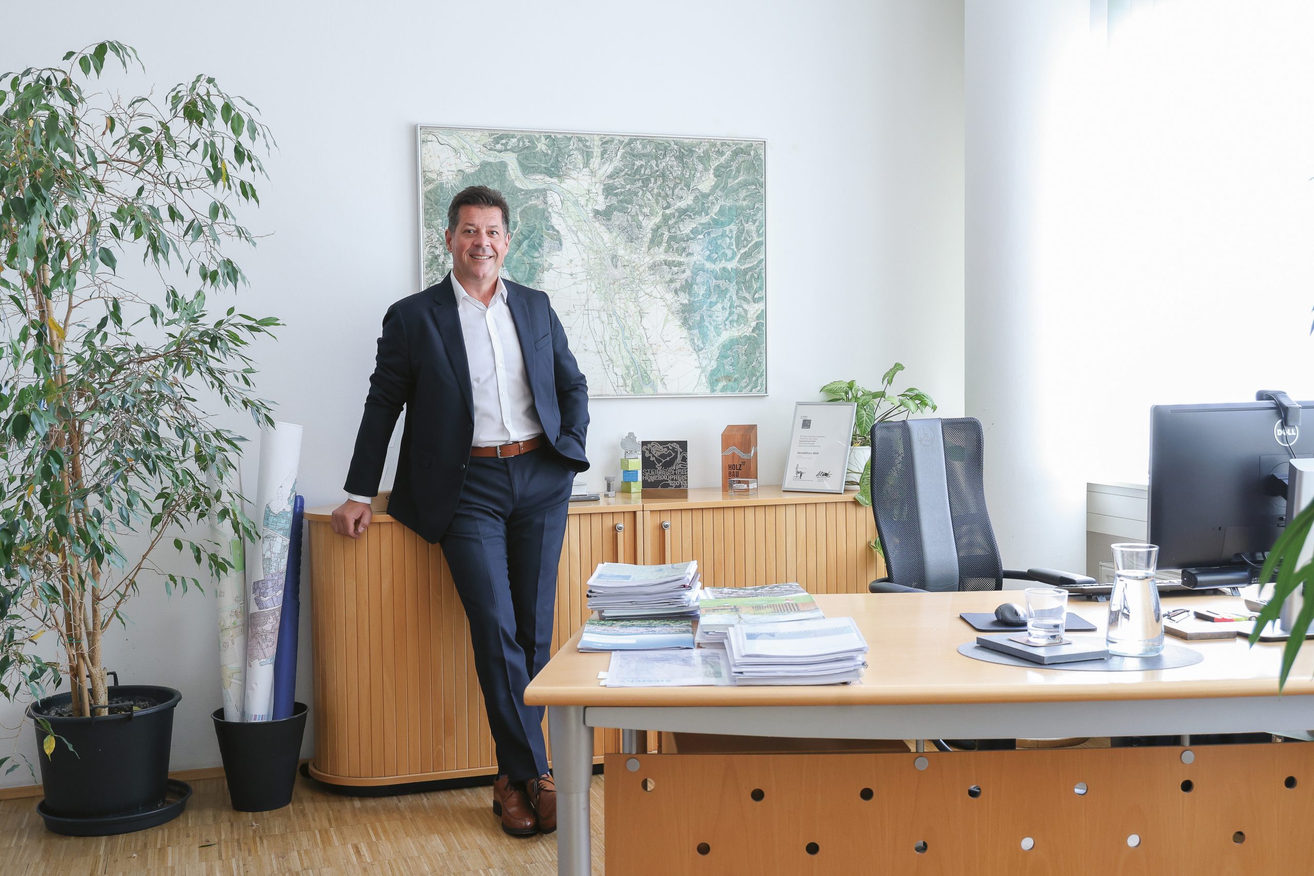 Ein Mann im Anzug, der in einem Büro steht und sich an einen Holzschrank lehnt.