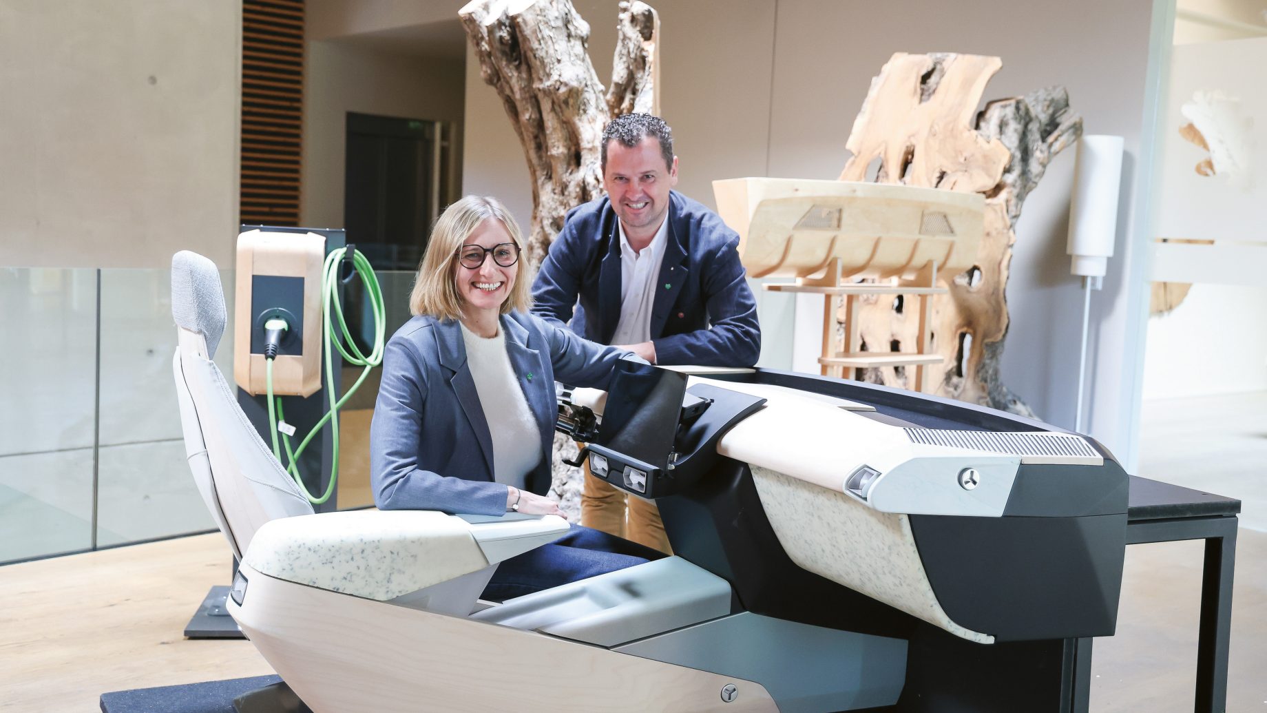 Eine Frau und ein Mann, die lächelnd hinter einem modernen, minimalistischen Cockpit-Display eines Fahrzeugs stehen.