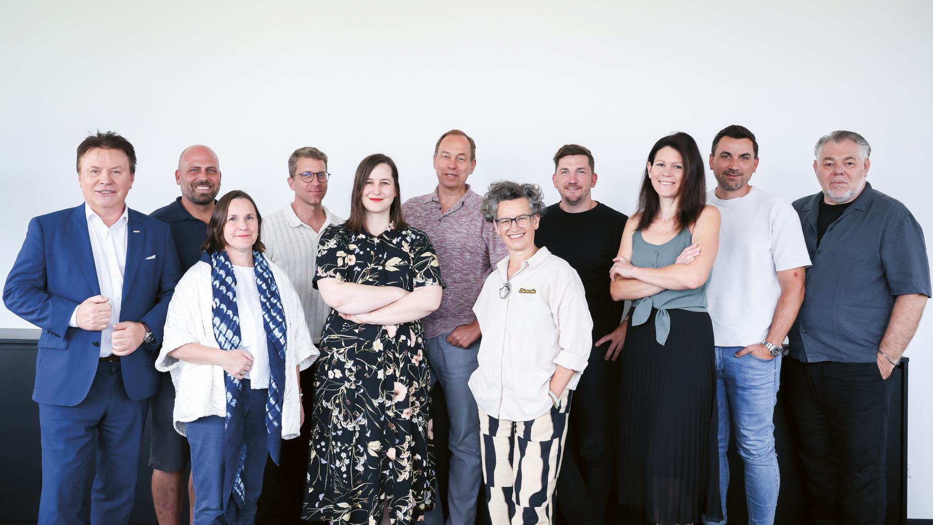 Eine Gruppe von elf Erwachsenen unterschiedlicher Herkunft posierte vor einer weißen Wand für ein Foto.
