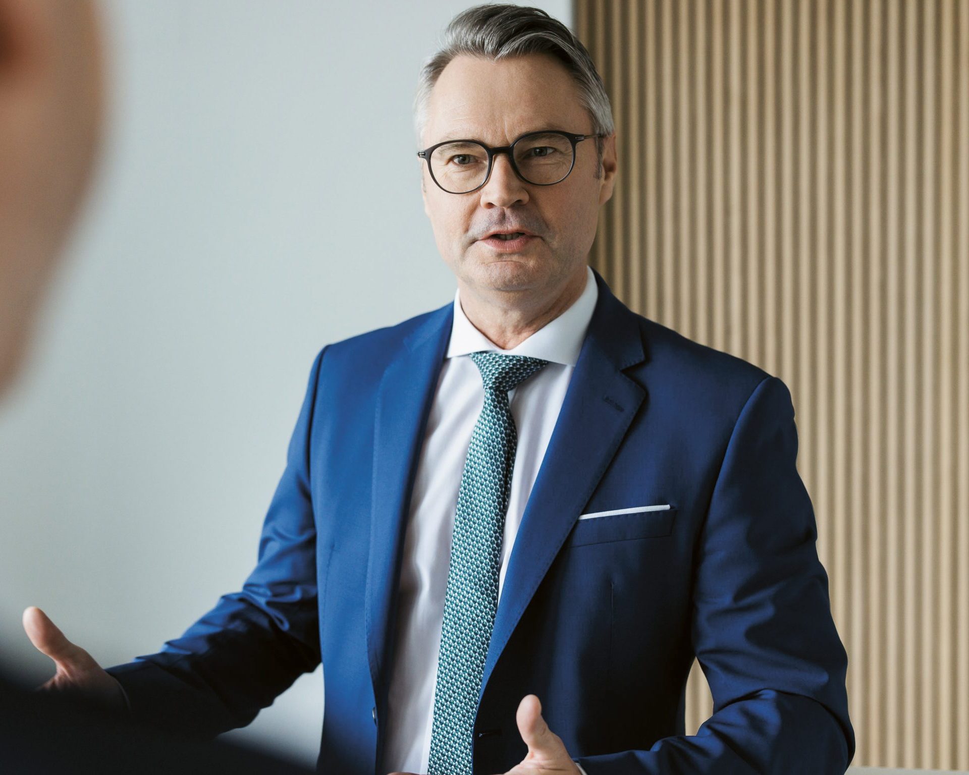 Ein Mann im Anzug und mit Brille, der mit jemandem außerhalb des Bildausschnitts spricht.