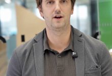 Ein Mann in einem grauen Blazer und einem braunen Poloshirt spricht in die Kamera.
