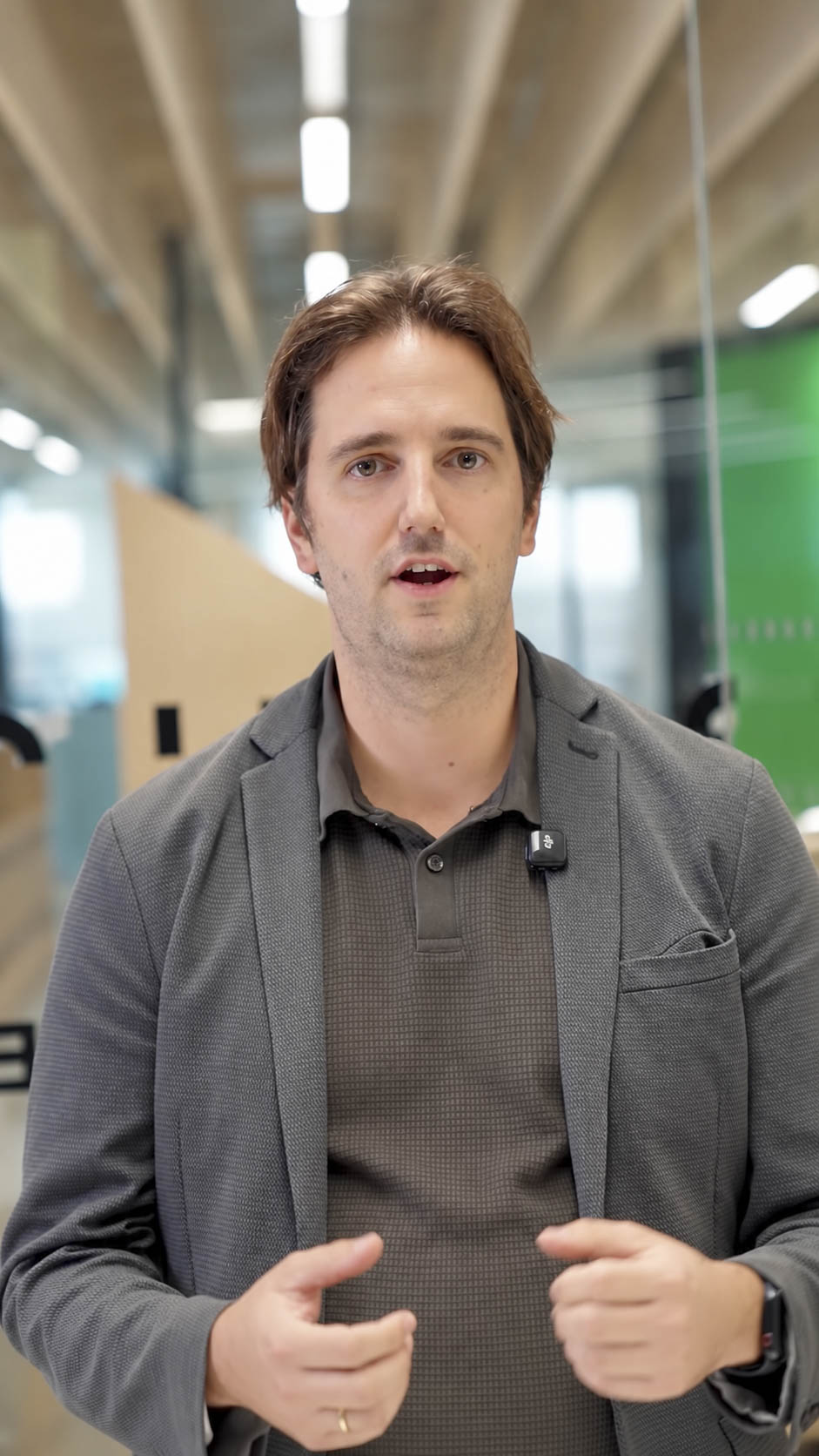 Ein Mann in einem grauen Blazer und einem braunen Poloshirt spricht in die Kamera.