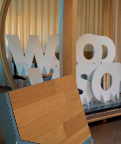 Hinter einer Ausstellungstheke des Wood Vision Lab stehen große weiße Buchstaben, die das Wort „WOOD“ bilden.