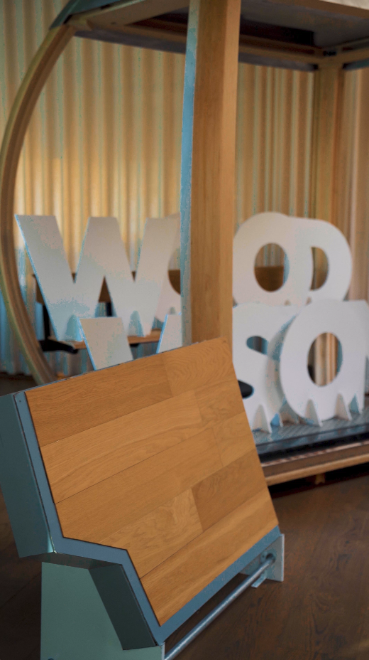 Hinter einer Ausstellungstheke des Wood Vision Lab stehen große weiße Buchstaben, die das Wort „WOOD“ bilden.