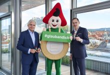 Zwei Männer in Anzügen stehen neben dem Sparefroh-Maskottchen und halten ein Schild von Klampfer Druck mit der Aufschrift „#glaubandich“ in den Händen.
