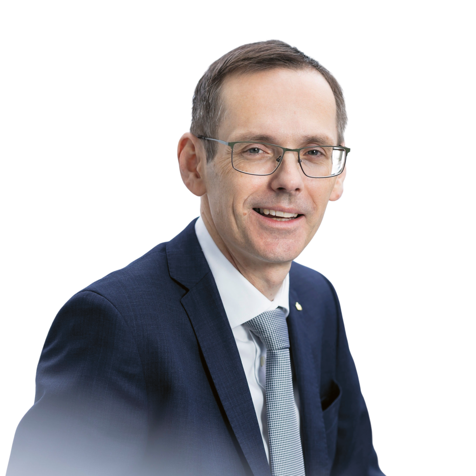 Ein Mann mittleren Alters mit kurzen Haaren und Brille, der einen dunklen Anzug, ein weißes Hemd und eine gemusterte Krawatte trägt.