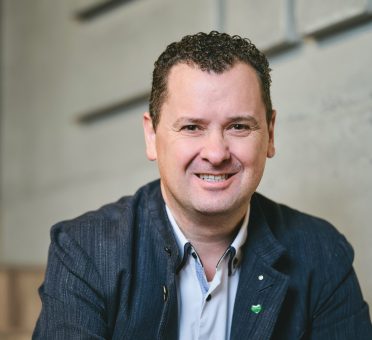 Ein lächelnder Mann, der einen Blazer und ein weißes Hemd trägt.